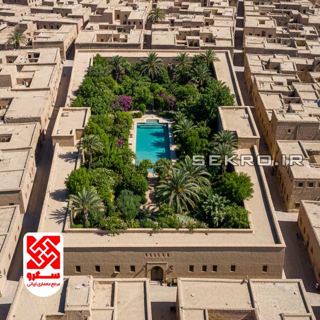 نمای عریض از بالا (Drone shot) به یک خانه حیاط‌دار در بافت کویری که مانند نگین سبزی در میان بافت خاکی می‌درخشد.