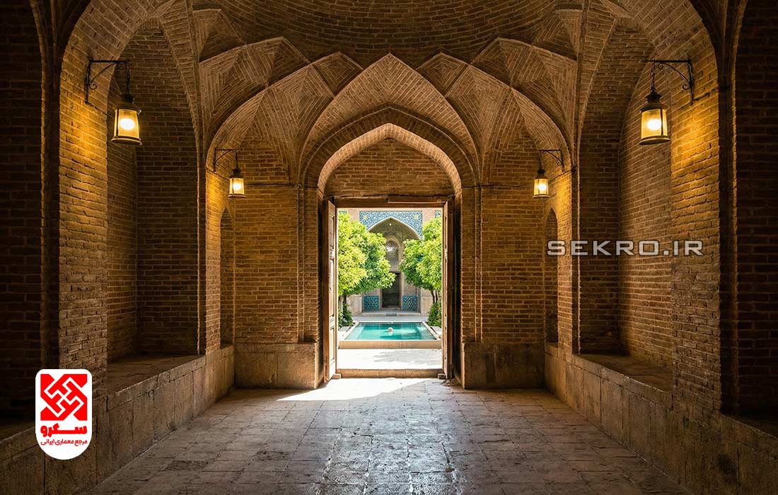 نمای عریض از هشتی ورودی خانه، نوری که از سقف می‌تابد و روزنه‌ای که حیاط سرسبز را نشان می‌دهد.